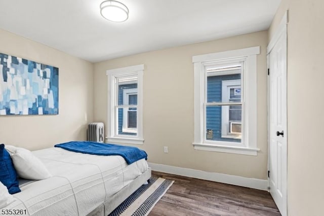 bedroom with radiator heating unit, baseboards, multiple windows, and wood finished floors