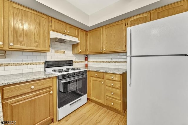 kitchen featuring white appliances, under cabinet range hood, light wood-style floors, decorative backsplash, and light stone counters