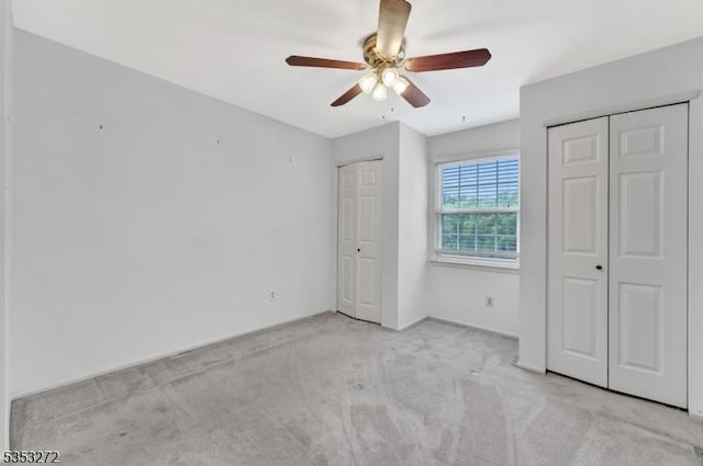 unfurnished bedroom with multiple closets, light carpet, and a ceiling fan