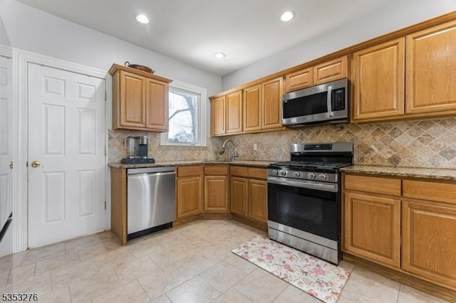 kitchen featuring brown cabinetry, appliances with stainless steel finishes, tasteful backsplash, a sink, and stone counters