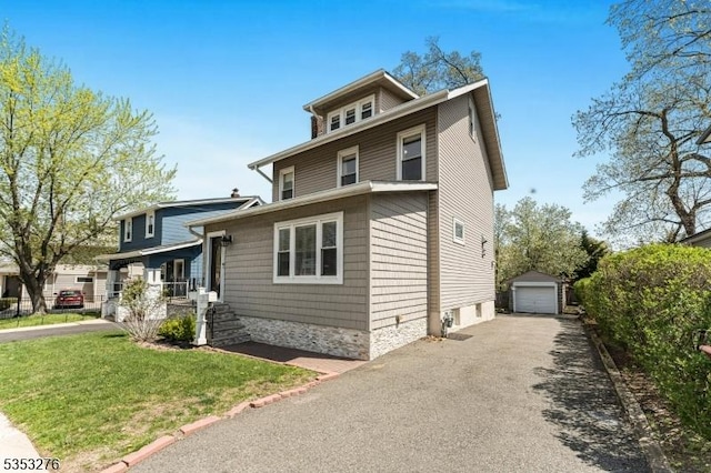 traditional style home with an outdoor structure, aphalt driveway, a front yard, and a detached garage