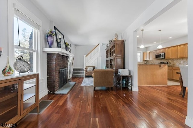 living area featuring baseboards, stairs, a brick fireplace, and wood finished floors
