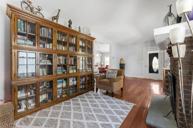 living area with a brick fireplace, baseboards, wood finished floors, and lofted ceiling