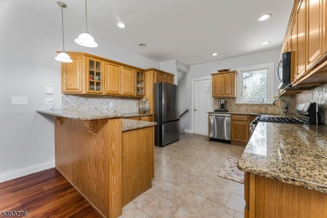 kitchen featuring a peninsula, light stone countertops, a kitchen bar, backsplash, and stainless steel appliances