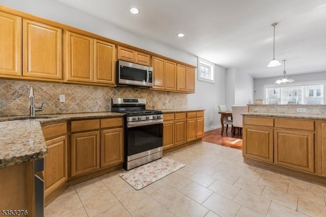 kitchen with backsplash, hanging light fixtures, a sink, light stone counters, and stainless steel appliances