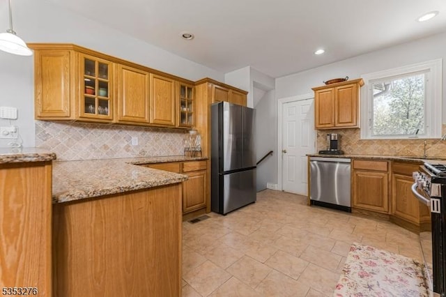 kitchen featuring brown cabinets, light stone counters, stainless steel appliances, backsplash, and glass insert cabinets