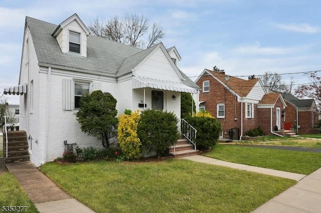 view of front of home featuring a shingled roof, a front lawn, and brick siding