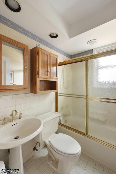 bathroom featuring toilet, enclosed tub / shower combo, and tile patterned flooring