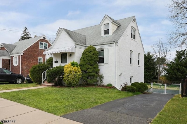 view of front of house with brick siding, a gate, a front lawn, and a shingled roof