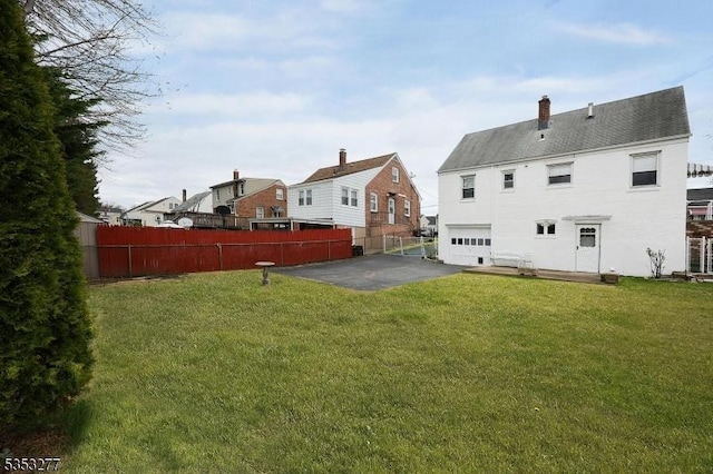 rear view of property with fence, an attached garage, a chimney, a patio, and a yard