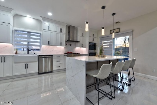 kitchen with a sink, backsplash, wall chimney range hood, a kitchen island, and appliances with stainless steel finishes