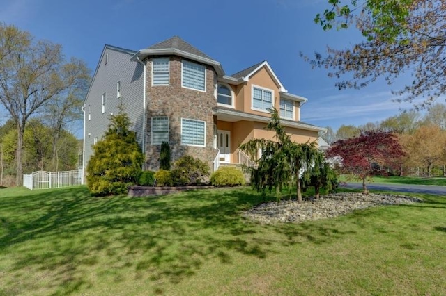 view of front facade featuring fence, a front lawn, and stone siding
