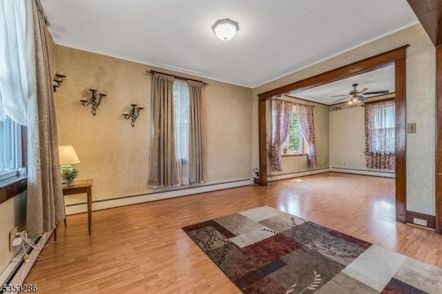 spare room with ceiling fan, baseboard heating, baseboards, wood finished floors, and ornamental molding