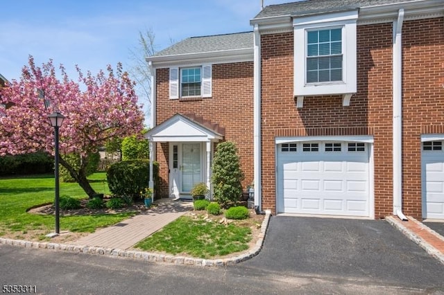townhome / multi-family property with a garage, aphalt driveway, roof with shingles, and brick siding