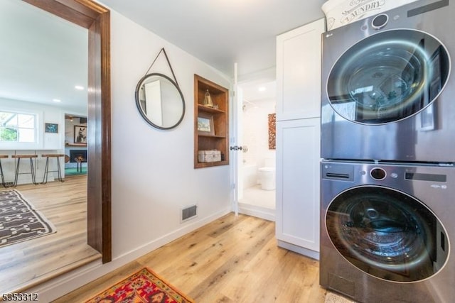 laundry room with light wood-style flooring, cabinet space, stacked washing maching and dryer, and visible vents
