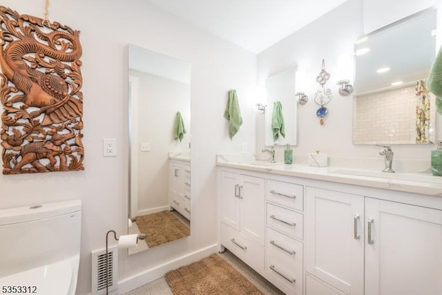 bathroom featuring visible vents, toilet, double vanity, and a sink