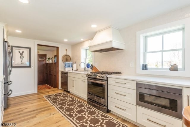 kitchen featuring a sink, custom exhaust hood, stainless steel appliances, and light wood-style floors
