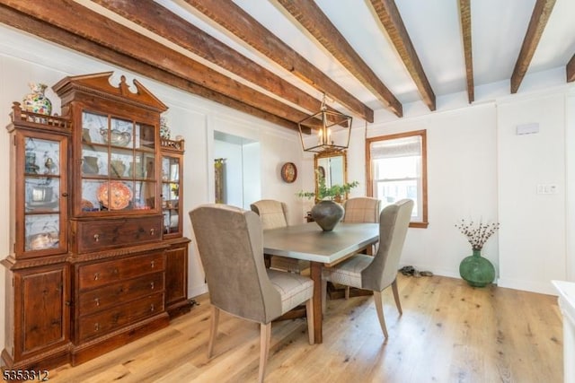 dining room with beam ceiling, baseboards, a notable chandelier, and light wood-style flooring