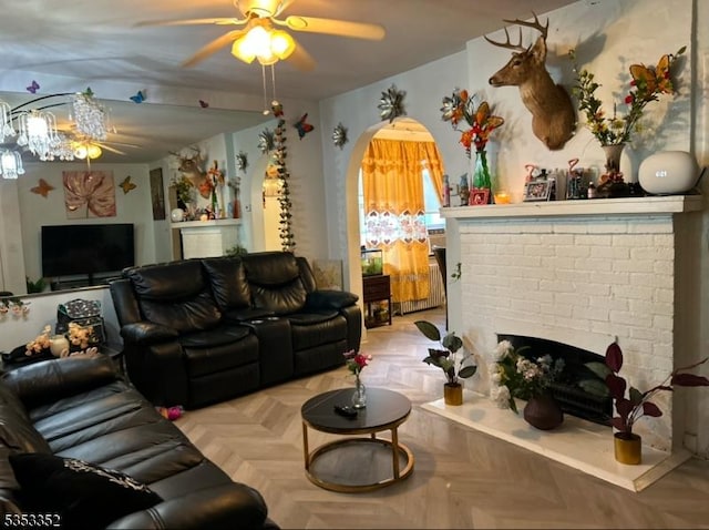 living area with a brick fireplace, arched walkways, and ceiling fan
