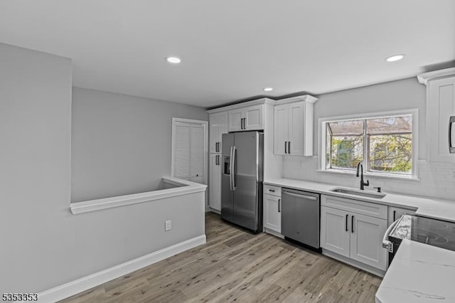 kitchen with appliances with stainless steel finishes, a sink, recessed lighting, light wood-style flooring, and decorative backsplash