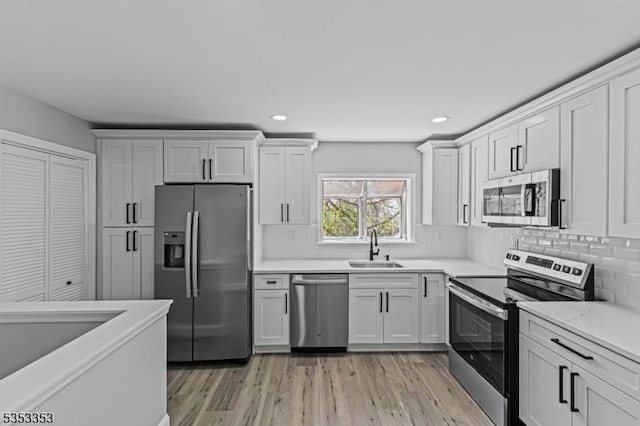 kitchen featuring stainless steel appliances, a sink, light wood-style flooring, backsplash, and recessed lighting