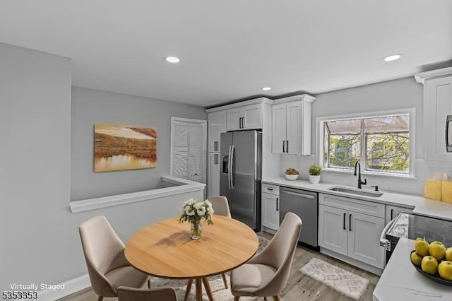 kitchen with stainless steel appliances, a sink, light countertops, recessed lighting, and light wood finished floors