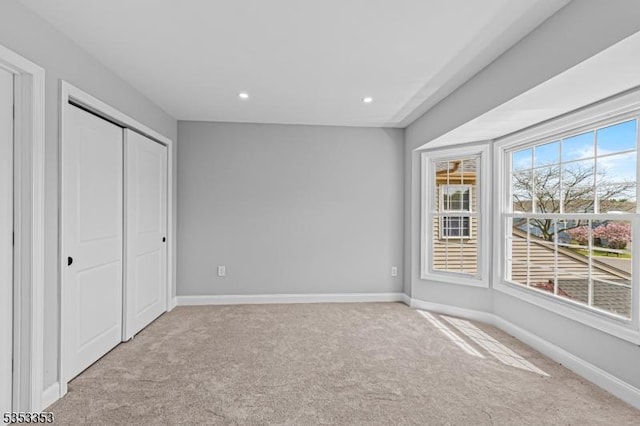 unfurnished bedroom featuring light colored carpet, baseboards, recessed lighting, and a closet