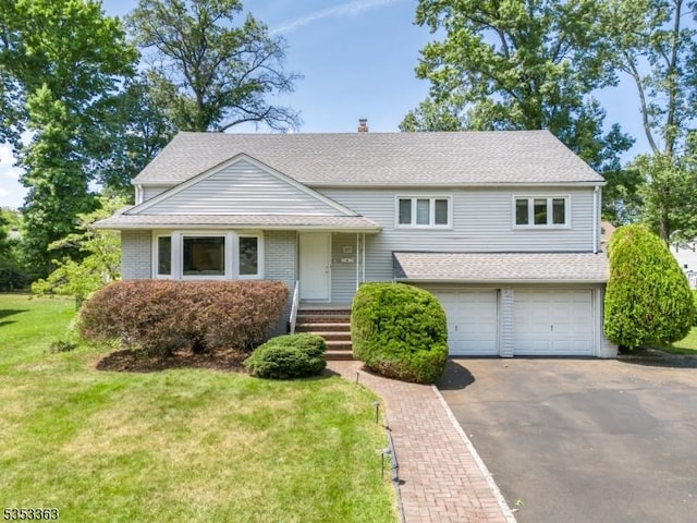 split level home with a garage, driveway, roof with shingles, and a front yard