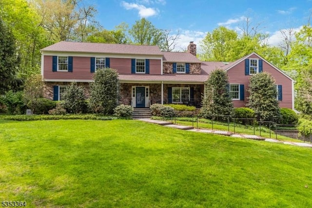 view of front of house featuring covered porch, a front yard, a chimney, and stone siding