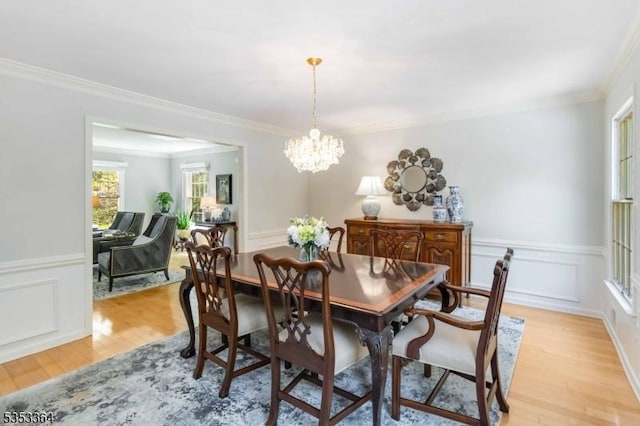 dining room with crown molding, an inviting chandelier, light wood-style floors, and wainscoting