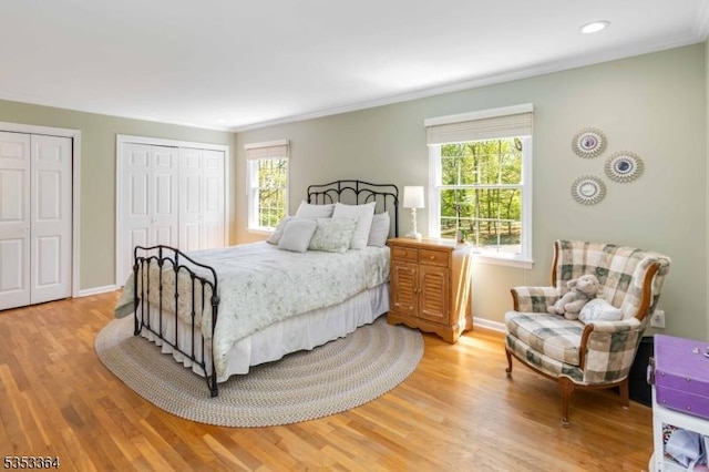 bedroom with multiple closets, baseboards, and light wood finished floors