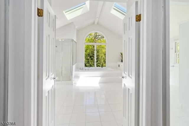 interior space featuring tile patterned flooring, a garden tub, a stall shower, and vaulted ceiling with skylight