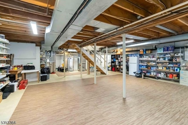unfinished basement with freestanding refrigerator, heating unit, gas water heater, and stairway