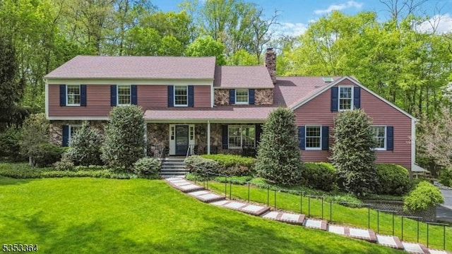 view of front of house with covered porch, a chimney, a front lawn, and stone siding