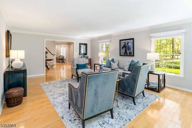living area with crown molding, baseboards, wood finished floors, and stairway
