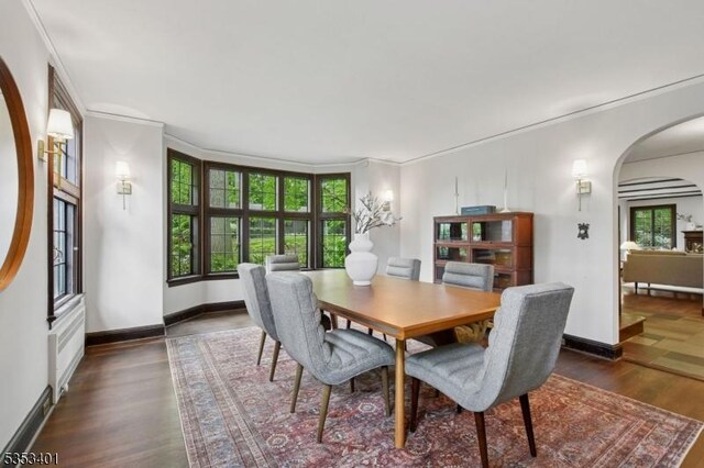 dining area with arched walkways, ornamental molding, wood finished floors, and baseboards