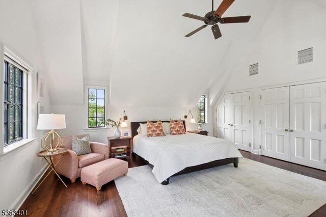 bedroom with high vaulted ceiling, wood finished floors, two closets, baseboards, and ceiling fan