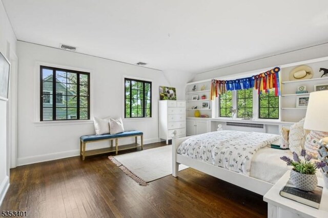 bedroom featuring wood finished floors, multiple windows, baseboards, and radiator heating unit