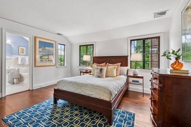 bedroom with wood finished floors, vaulted ceiling, baseboards, and ensuite bathroom