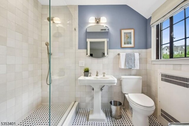 bathroom featuring radiator heating unit, tiled shower, toilet, tile patterned flooring, and a wainscoted wall