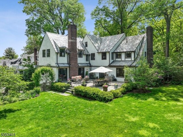 back of property with stucco siding, a high end roof, a chimney, and a lawn