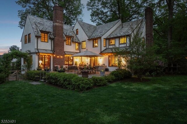 rear view of property with a high end roof, stucco siding, a lawn, a chimney, and a patio