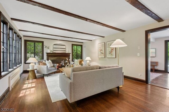 living room featuring beamed ceiling, wood finished floors, baseboards, and a lit fireplace