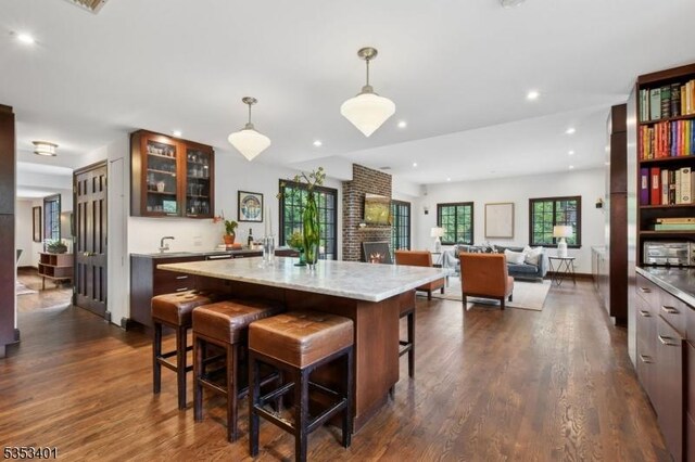 kitchen featuring a kitchen breakfast bar, glass insert cabinets, dark wood finished floors, hanging light fixtures, and recessed lighting