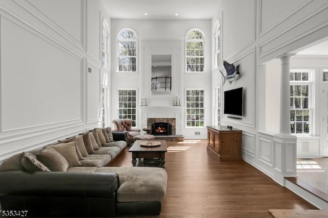 living area featuring a fireplace, a decorative wall, decorative columns, wood finished floors, and a towering ceiling