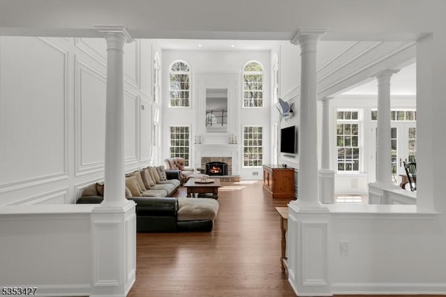 living area featuring a towering ceiling, a lit fireplace, dark wood-style floors, and a decorative wall