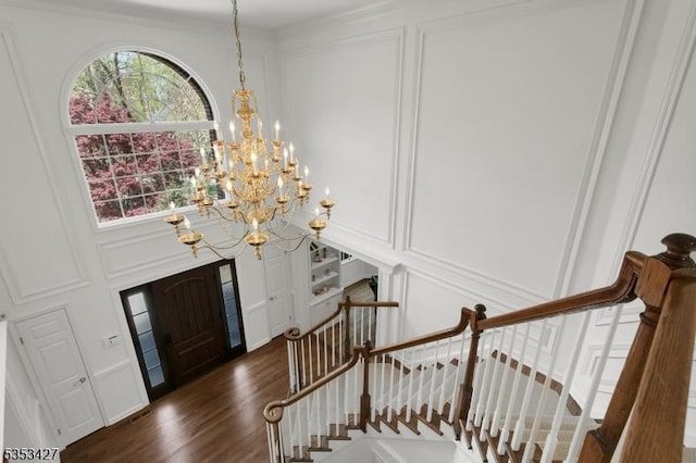 entrance foyer featuring stairway, a decorative wall, dark wood-style floors, and a chandelier