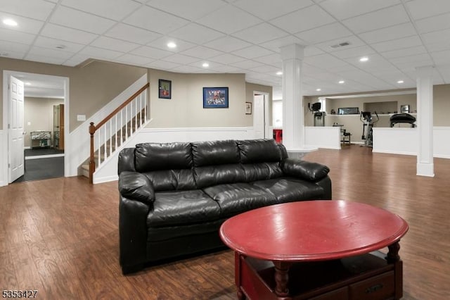 living room featuring stairs, a drop ceiling, wood finished floors, ornate columns, and visible vents