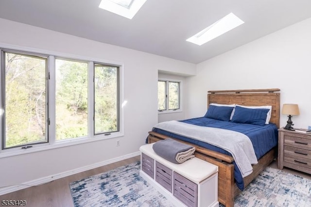 bedroom with baseboards, vaulted ceiling with skylight, and light wood-type flooring