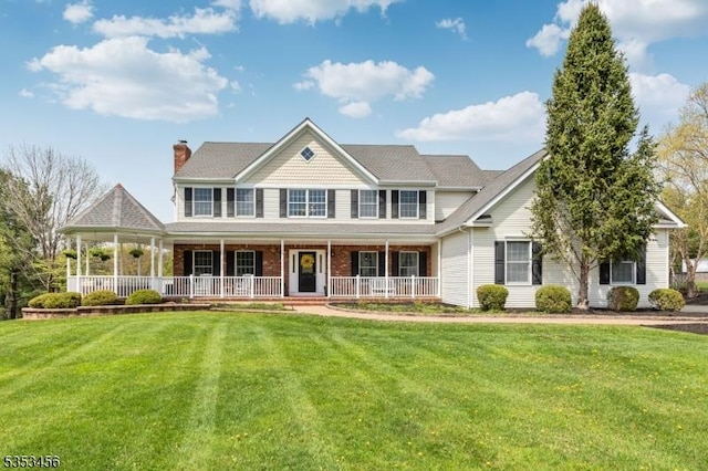 view of front of home featuring a chimney, a porch, a front lawn, and brick siding